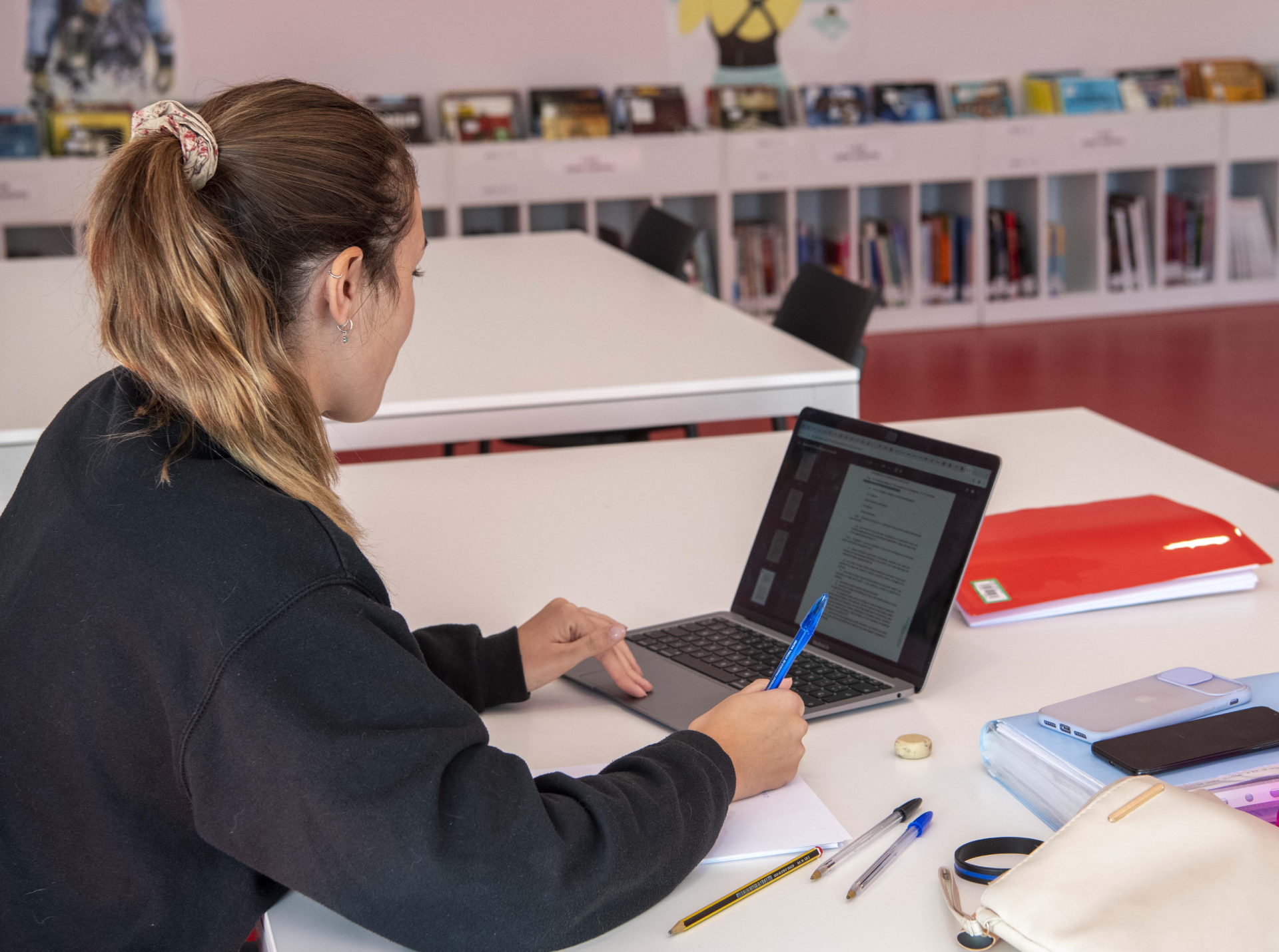Una joven consulta información en un portátil, sentada en una mesa de una biblioteca