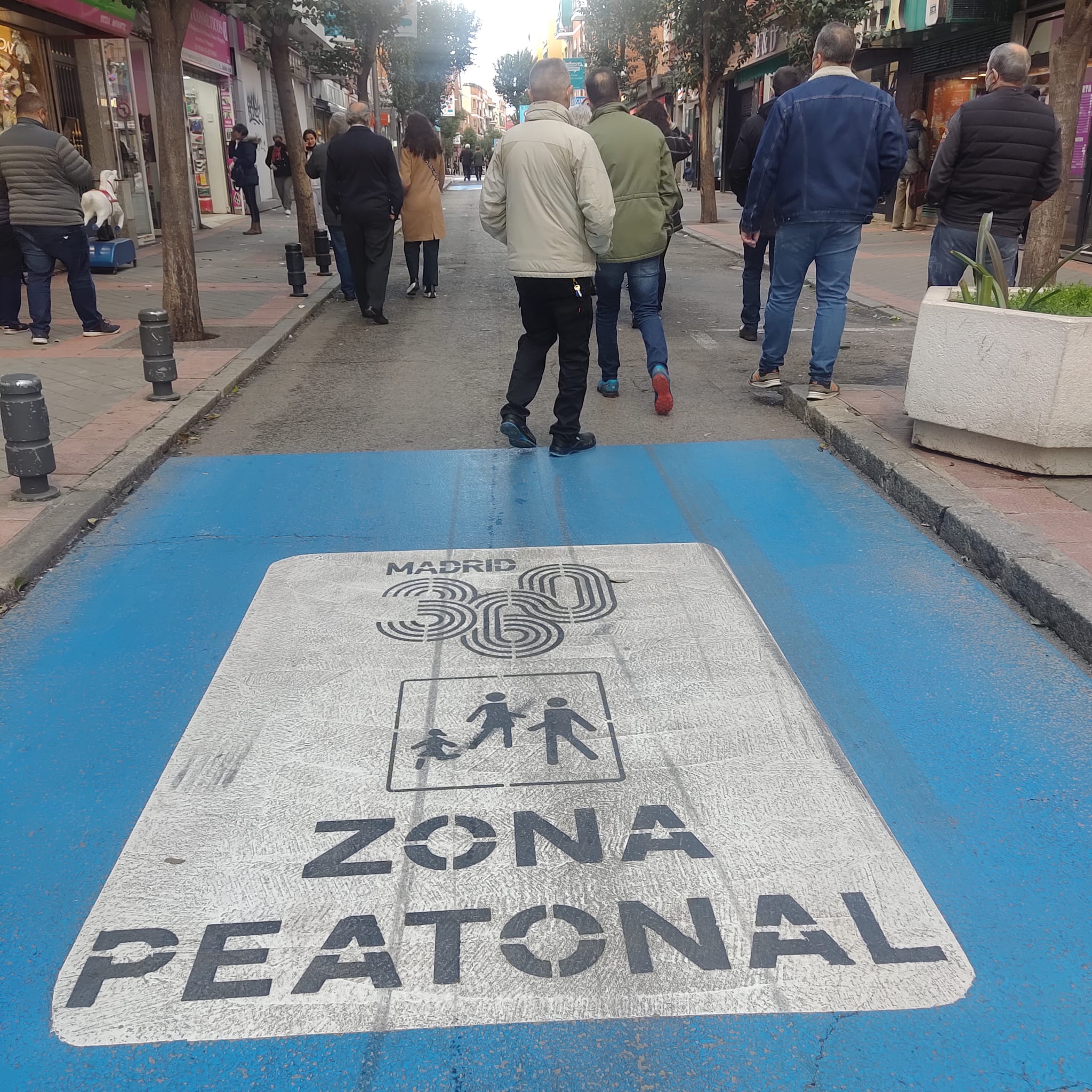 Varias personas caminan sobre el asfalto de la calle de la Laguna. En el suelo se ve una señal pintada que indica Zona peatonal.