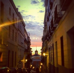 En la calle de San Cosme y San Damián, el sol se desviste de su manto dorado. Las sombras se alargan, como susurros de los siglos pasados, y el cielo se tiñe de naranja y rosa, como un lienzo de sueños.