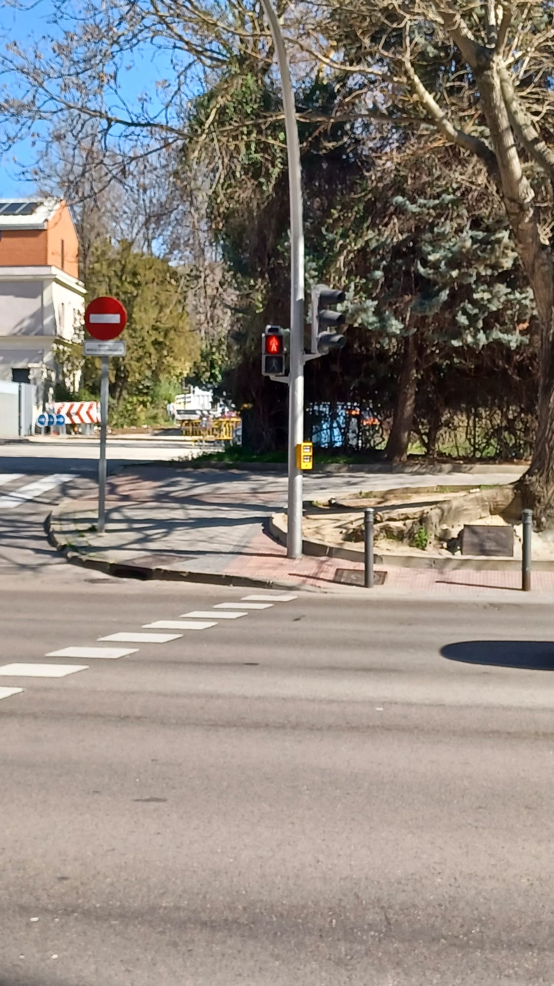 Como puede observarse, el espacio habilitado para la espera es reducido, presenta una pendiente considerable y no reúne condiciones adecuadas de seguridad para el tránsito y la permanencia de peatones. Esta circunstancia genera una situación de especial riesgo para personas usuarias con carritos infantiles, así como para menores de edad.

Además, debe tenerse en cuenta que este punto se encuentra situado junto a una avenida con elevada intensidad de tráfico y en las inmediaciones de la salida de un centro escolar y una guardería, lo que provoca que, en determinadas franjas horarias, se concentre un número significativo de personas en espera para cruzar.

En consecuencia, la ubicación actual del semáforo puede resultar insuficiente desde el punto de vista de la seguridad peatonal y de la adecuada gestión de los flujos de paso, por lo que se considera conveniente valorar su modificación o reubicación.
